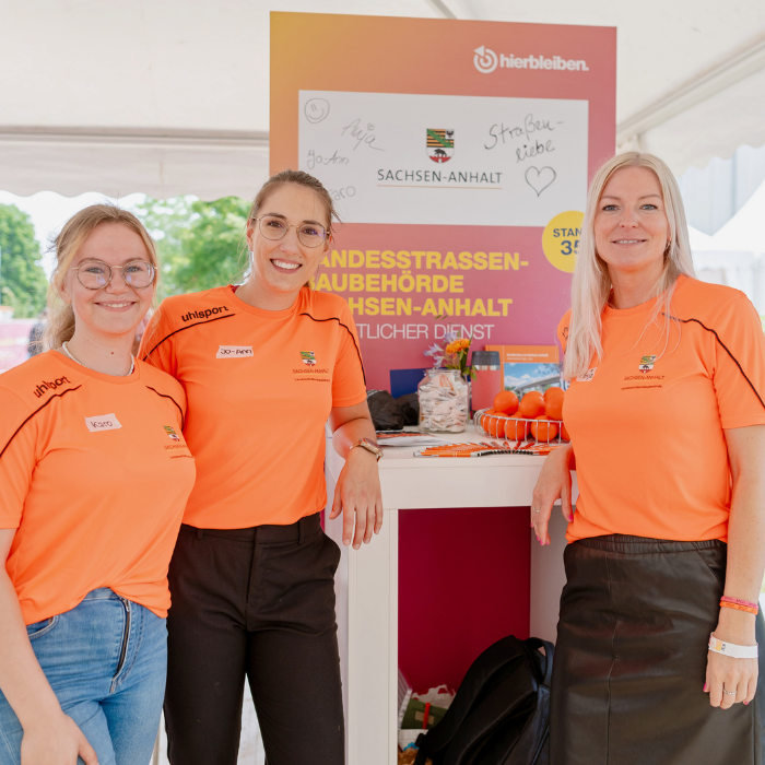 Drei Personalrecruiterinnen stehen an einem Messestand. 