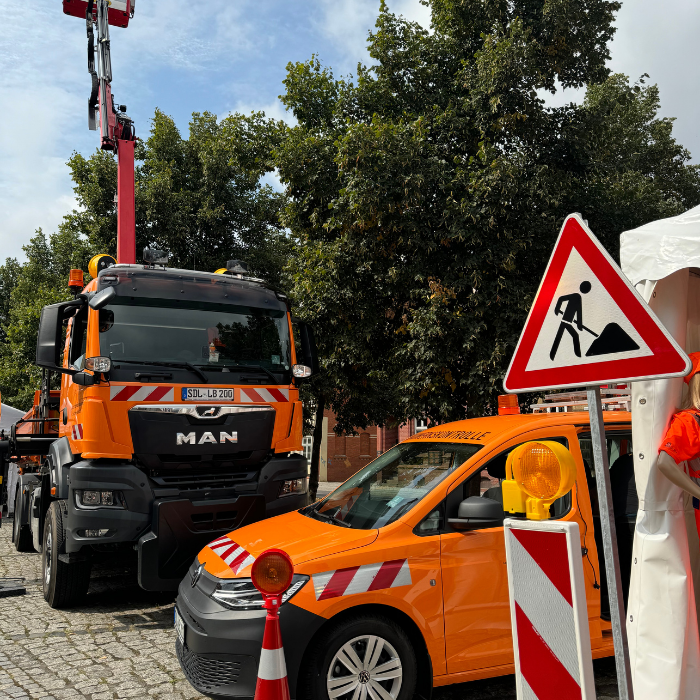 Zwei orangefarbene Fahrzeuge des Betriebsdienstes der LSBB sowie ein Baustellenschild und eine Bake sind sichtbar. 
