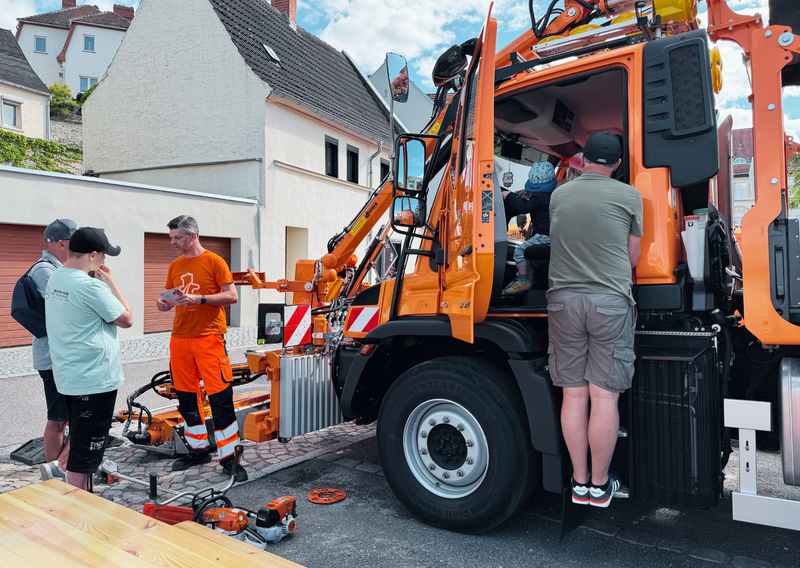 Unimog im Hintergrund, Betriebsdienstler unterhalten sich mit Interessenten