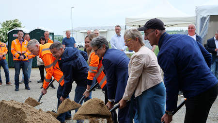Menschen mit Spaten in der Hand bewegen Sand, um symbolisch den Spatenstich einzuleiten. 