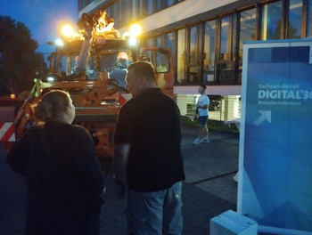 Vor einem Unimog stehen ein Aufsteller und Besucher der Langen Nacht der Wissenschaft. 