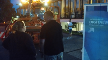 Vor einem Unimog stehen ein Aufsteller und Besucher der Langen Nacht der Wissenschaft. 